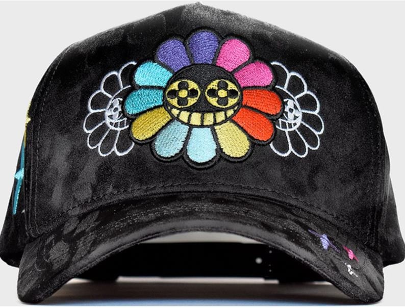 May include: A black velvet baseball cap featuring a large, central embroidered flower with multi-colored petals and a smiling face with four-leaf clover eyes. Two smaller, white-outlined flower silhouettes flank the central design.