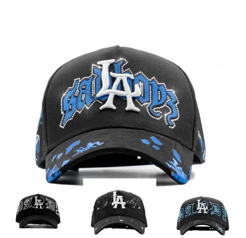 May include: Black baseball cap with the text "LA BADDS" in white and blue. The cap features a curved brim and a decorative design on the front. The hat is a stylish accessory.