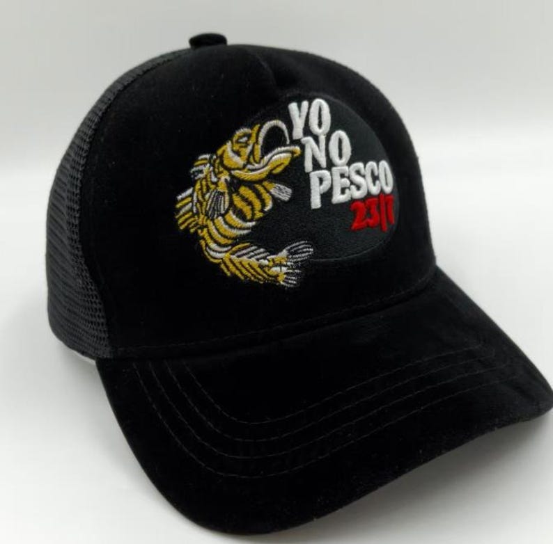 May include: Black baseball cap with a mesh back and a curved peak. The front has an embroidered patch with a yellow and black fish design and the text "YO NO PESCO 2310".