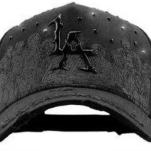 May include: Black baseball cap with a curved brim. The cap features the letters "LA" in a stylized design on the front. The cap has a textured pattern and small studs on the crown.