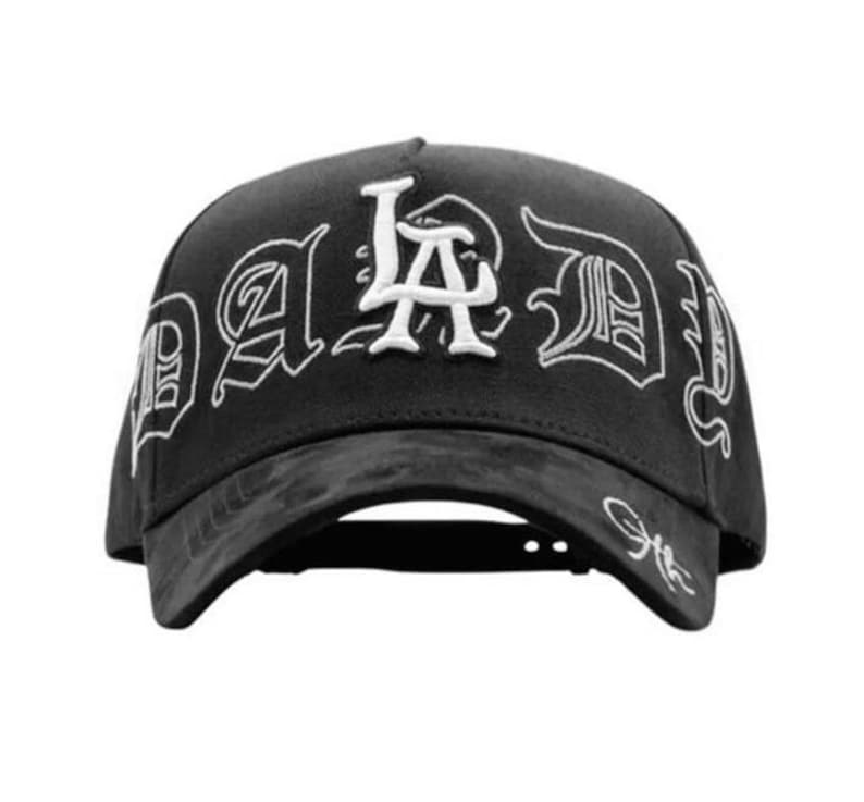 May include: Black baseball cap featuring the white embroidered text "LA Dad" in a gothic font. The cap has a curved peak and a textured finish.