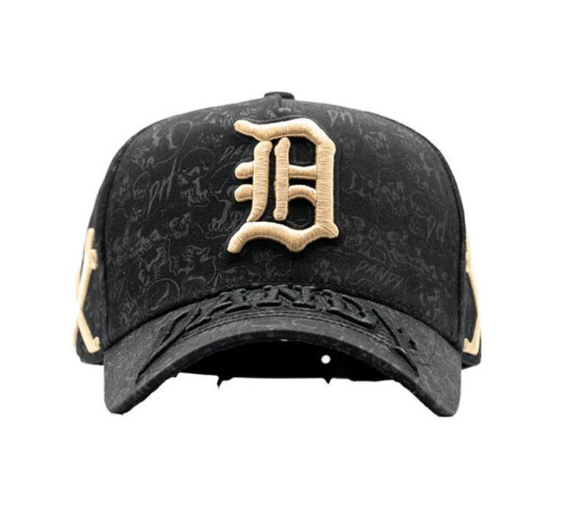 May include: Black baseball cap with a gold embroidered letter "D" on the front. The cap has a textured pattern and gold accents on the sides. The brim features embossed text.