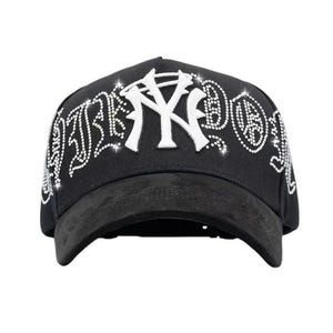 May include: Black baseball cap featuring a white "NY" logo and rhinestone detailing. The curved peak is a dark grey suede-like material. The word "NY" is in a bold, stylized font.