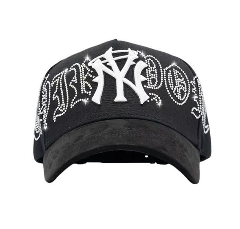 May include: Black baseball cap featuring a white "NY" logo and rhinestone detailing. The curved peak is a dark grey suede-like material. The word "NY" is in a bold, stylized font.