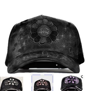 May include: A black baseball cap featuring a large embroidered flower design on the front panel. The flower has a sad face with stitched eyes and a mouth. The cap has a distressed, textured finish and includes smaller floral outlines on the sides.