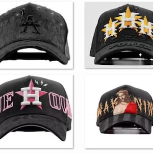 May include: Four black baseball caps with embroidered designs. One features the letters "LA", another has gold and white starbursts, a third displays "JE HOU", and the last depicts a religious figure.