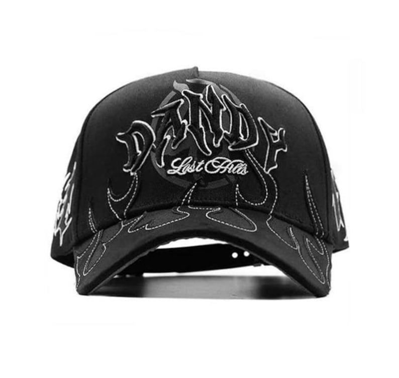May include: Black baseball cap with white embroidered flames and text. The cap features the text "Dandy" in a stylized font above "Lost Hills". The brim and sides have flame designs.