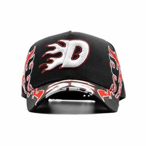 May include: Black baseball cap with a white and red embroidered flame design. The cap features a white letter "D" with a red outline, and flame accents on the sides and brim. A stylish accessory.