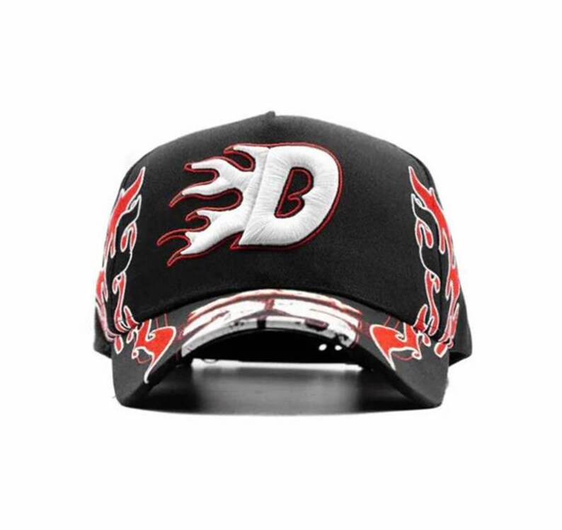 May include: Black baseball cap with a white and red embroidered flame design. The cap features a white letter "D" with a red outline, and flame accents on the sides and brim. A stylish accessory.
