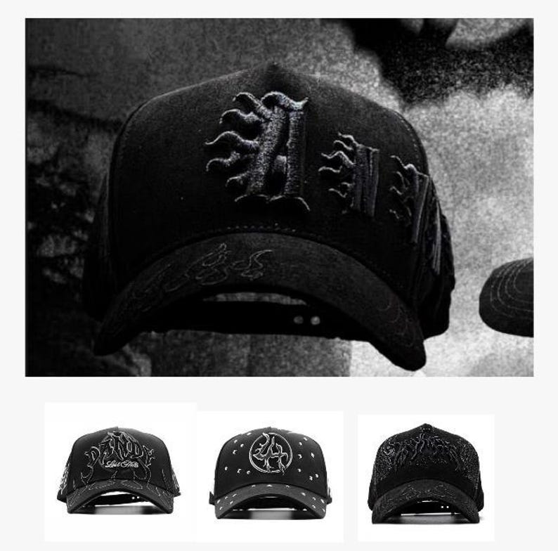 以下が含まれることがあります： 刺繍が施された黒い野球帽。帽子には装飾的な文字「A」とその他の装飾要素があります。つばとクラウンにも複雑なデザインが施されています。全体的な美しさは暗く、詳細です。