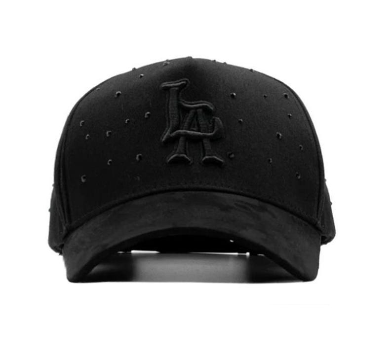 May include: Black baseball cap featuring the letters "LA". The cap has a curved peak and small, decorative studs. The hat is made of a suede-like material. The cap is a stylish accessory.