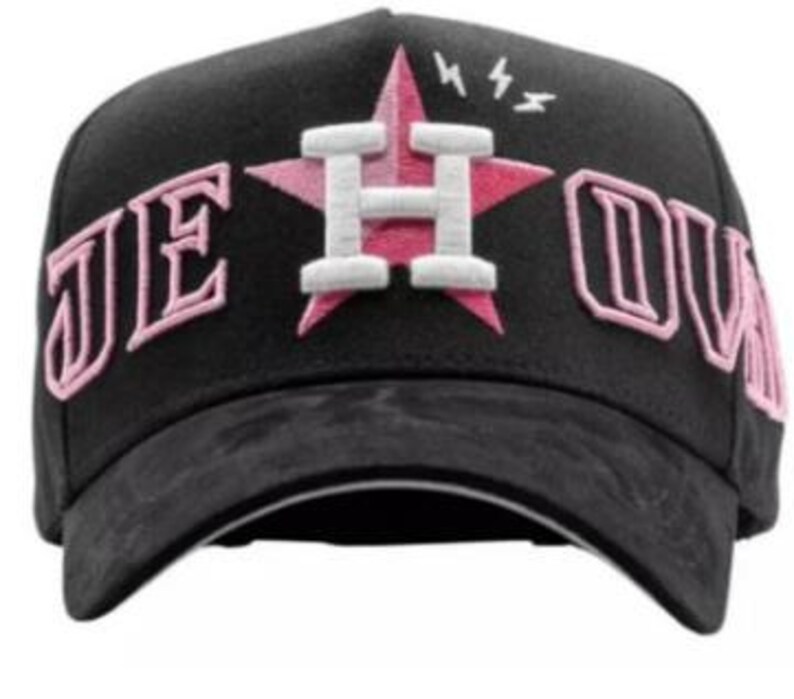 May include: Black baseball cap with a pink star and the letter "H" in white. The text "JE OUV" is embroidered in pink on the cap. The brim is black.