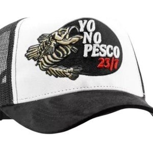May include: A black and white trucker cap with a mesh back. The front panel displays a fish skeleton graphic and the text "YO NO PESCO 23/7" in white and red.