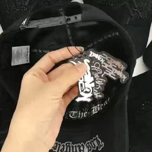 K&ouml;nnte beinhalten: Eine schwarze Baseballkappe mit verstellbarem Snapback-Verschluss, einem inneren Schwei&szlig;band mit dem Text The Best und einem wei&szlig;en Pflegeetikett. An der Kappe sind mehrere schwarz-wei&szlig;e Papieranh&auml;nger mit grafischen Textdesigns befestigt.