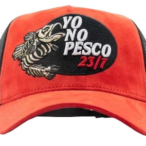 May include: Red and black trucker hat with a fish graphic and the text "YO NO PESCO 23/7". The hat has a red front panel, a black mesh back, and a curved peak.