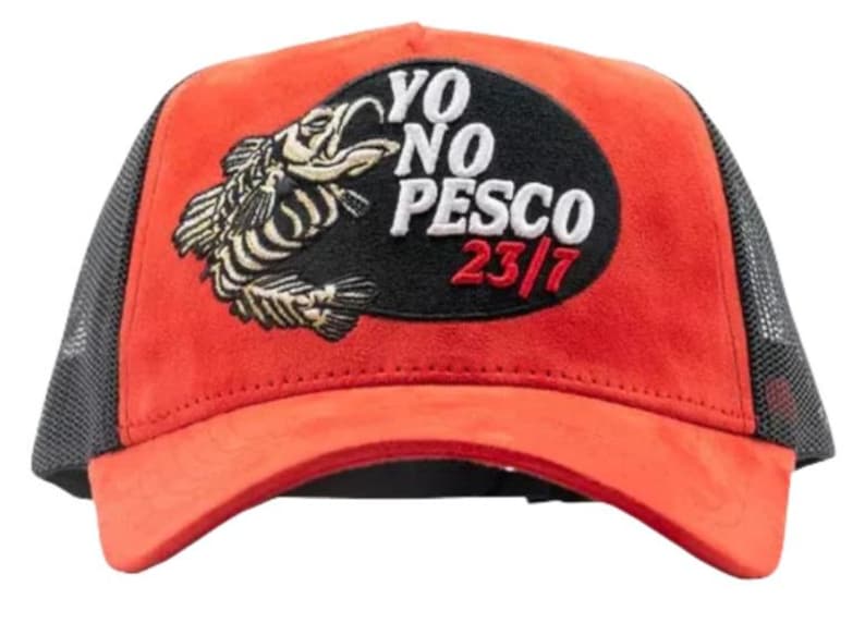 May include: Red and black trucker hat with a fish graphic and the text "YO NO PESCO 23/7". The hat has a red front panel, a black mesh back, and a curved peak.