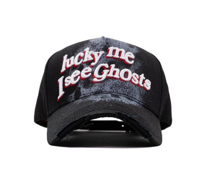 May include: Black baseball cap with a distressed finish. The cap displays the embroidered text "lucky me I see Ghosts" in white and red. It has a curved peak and an adjustable strap at the back.
