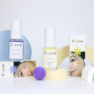 May include: Two Dermi Paris serum bottles, one with blue liquid labeled Phyto-Retinol and one with yellow liquid labeled Vita Glow, alongside their respective white rectangular boxes featuring facial imagery and floral icons, plus a purple sphere.