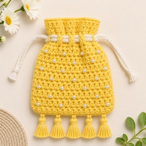 May include: A bright yellow crochet drawstring pouch featuring a textured stitch pattern embellished with small white faux pearls. The pouch includes a thick white braided cord closure and five matching yellow tassels hanging from the bottom edge.