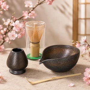 Puede incluir: Un juego de té matcha que incluye un soporte para batidor de cerámica marrón oscuro, un batidor de bambú en un estuche cilíndrico transparente, un cuenco vertedor de cerámica marrón oscuro texturizado y una cuchara de bambú curva.