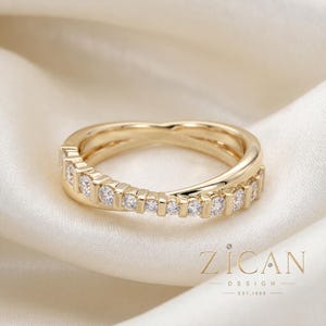 May include: A gold ring featuring a crossover band design with a row of small, round, clear, faceted stones set along one side. The text ZICAN DESIGN EST. 1998 is visible in the lower right corner of the image.