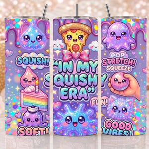 May include: A cylindrical tumbler with a straw featuring a purple background covered in glittery, colorful cartoon characters, including a pizza slice, a rainbow cake, and a ghost, with the text "IN MY SQUISHY ERA," "SQUISH," and "GOOD VIBES."