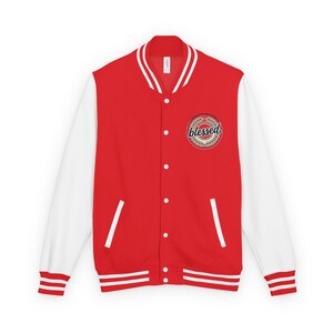 May include: A red varsity jacket with white sleeves, featuring a ribbed collar, cuffs, and hem with white stripes. The front has a snap-button closure and two side pockets. A circular emblem on the left chest displays the word blessed in script.