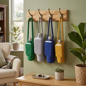 May include: Four crochet bottle holders in green, gray, blue, and yellow, each featuring a small front pocket and a long strap. These holders are hanging from a light wood wall rack with four metal hooks, each containing a silver metal water bottle.