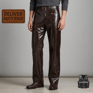 May include: Dark brown trousers featuring a glossy, embossed crocodile skin texture. The pants have a straight-leg cut, a button and zipper fly, and classic five-pocket styling. A brown rectangular badge reads DELIVER DUTY PAID.