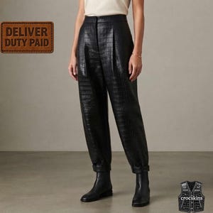 Puede incluir: Pantalones negros de talle alto con un patrón texturizado de piel de cocodrilo, cierre de cremallera frontal y silueta de pierna cónica con dobladillos vueltos. La prenda se combina con botines de cuero negro y una parte superior color crema.