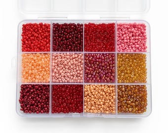 Pode incluir: Um recipiente de armazenamento de plástico transparente com doze compartimentos retangulares preenchidos com pequenas contas de vidro redondas em vários tons de vermelho, rosa, laranja e dourado. Cada seção contém uma cor uniforme.