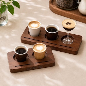 Könnte beinhalten: Zwei rechteckige Serviertabletts aus dunklem Holz mit kreisförmigen Aussparungen für Kaffeetassen. Ein Tablett enthält drei Tassen, darunter eine weiße, eine dunkelbraune und ein Glas mit Kaffee. Das andere Tablett enthält zwei Tassen, eine braune und eine beige.