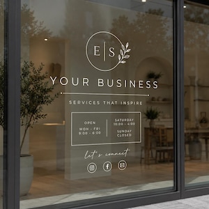 以下が含まれることがあります： 白いグラフィックデザインのショーウィンドウ。デザインには「YOUR BUSINESS」、「SERVICES THAT INSPIRE」の文字と営業時間、ソーシャルメディアのアイコンが含まれています。窓は黒いフレームで囲まれています。