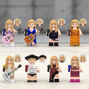 May include: A collection of Lego-style figurines, each depicting a blonde woman with a microphone. Some figures hold guitars, while others wear various outfits, including a dress, a bodysuit, and a t-shirt with the text "A LOT GOING ON AT THE MOMENT."