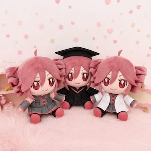May include: Three plush dolls with pink hair and large red eyes. The left doll wears a grey outfit, the centre doll wears a black graduation cap and gown, and the right doll wears a white lab coat over a grey outfit. All dolls have pink accents.