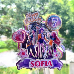 Könnte beinhalten: Ein mehrschichtiger Tortenaufleger mit drei animierten Figuren, einer Herzform und einem kreisförmigen Emblem mit der Zahl 7. Das Design enthält den Text Happy Birthday und den Namen SOFIA auf einem violetten Banner, akzentuiert durch glitzernde Sterne.