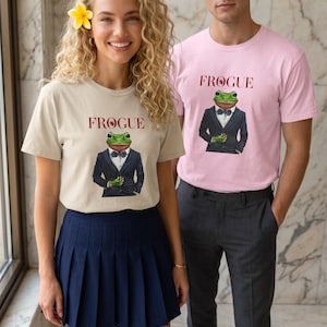 Könnte beinhalten: Ein beiges T-Shirt und ein hellrosa T-Shirt, beide mit einer Grafik eines grünen Frosches in einem schwarzen Smoking mit Fliege und dem darüber gedruckten Text FROGUE. Die T-Shirts haben kurze Ärmel und einen Rundhalsausschnitt.