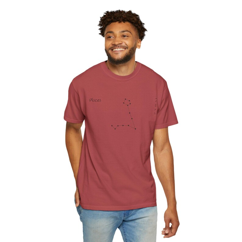 A man wearing a reddish-brown t-shirt with "Pisces" and the Pisces constellation printed in black, standing against a white background.
