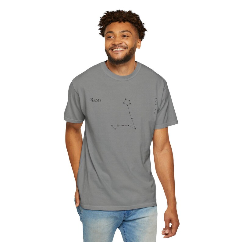 A man in a gray t-shirt with "Pisces" and the Pisces constellation printed in black, standing with one hand in his pocket.