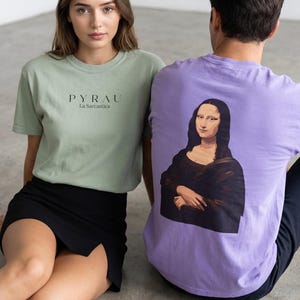 A woman in a light green t-shirt with "PYRAU La Sarcastica" printed on the front sits next to a man in a purple t-shirt with a Mona Lisa graphic on the back.