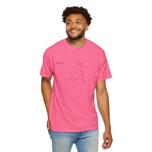 A man wearing a hot pink t-shirt with "Pisces" and the Pisces constellation printed in black, standing against a white background.