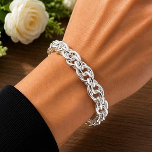May include: A polished silver chain bracelet featuring a series of interlocking oval links. The bracelet has a bright, reflective metallic finish and is secured around the wrist, showcasing a classic, uniform design with consistent link sizing.