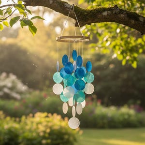 May include: A hanging mobile featuring multiple circular discs in varying shades of blue, teal, and white. The discs are suspended from a circular wooden frame by thin white strings, creating a layered, cascading arrangement of translucent elements.