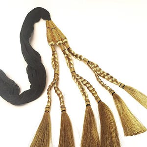 May include: A decorative tassel accessory featuring a thick black cord that splits into three braided gold metallic strands. Each braided section terminates in a long, flowing gold fringe tassel, with small gold-wrapped accents securing the braids.