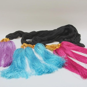 May include: A black cord featuring multiple decorative tassels in shades of purple, bright blue, and hot pink. Each tassel is attached to the black cord with a gold-colored metal cap. The text CATFLUFF is printed in the bottom right corner.