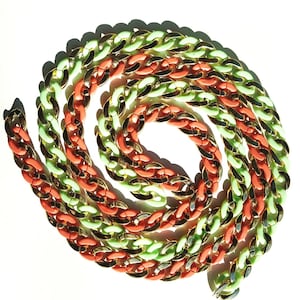 May include: A coiled chain necklace featuring alternating thick links in matte neon green and coral orange, interspersed with polished gold-tone metal links. The chunky, interlocking design creates a circular pattern with a vibrant color palette.