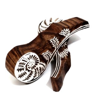 May include: Two dark brown wooden printing blocks featuring intricate carved designs of a spiraling fern frond. The raised surfaces of the wood are highlighted in white, showcasing the detailed botanical patterns and curved shapes of the stamps.
