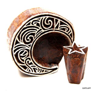 May include: A dark brown wooden printing block shaped like a crescent moon with intricate carved swirl patterns and a separate smaller dark brown wooden printing block shaped like a five-pointed star. The text CATFLUFF is printed in the bottom right.
