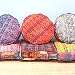 以下が含まれることがあります： 紫、オレンジ、白の複雑な模様が施された3つの円形フロアクッションと、その下に配置されたピンク、濃い紫、黄色の色合いのパッチワークデザインと詳細な刺繍が施された3つの正方形のフロアクッション。