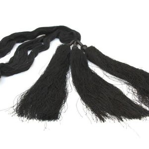 May include: A black decorative tassel accessory featuring three long, thin, dangling fringe segments attached to a central cord. The cord is looped and twisted, leading to a knot that secures the three individual black fiber tassels together.